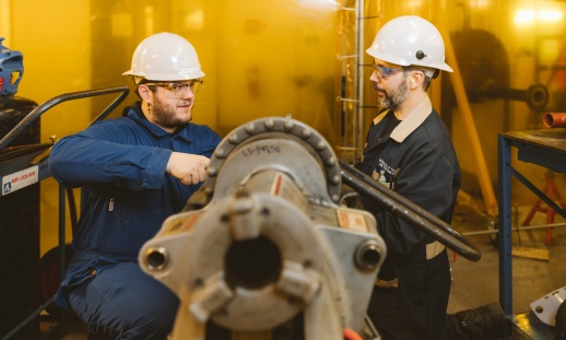Two people working on a large pipe in a training facility.
