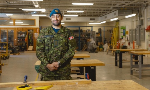 A person in uniform standing in a carpentry classroom.