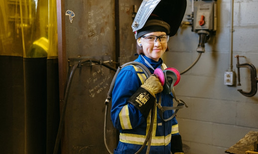 A person in welding attire smiling in a workshop.