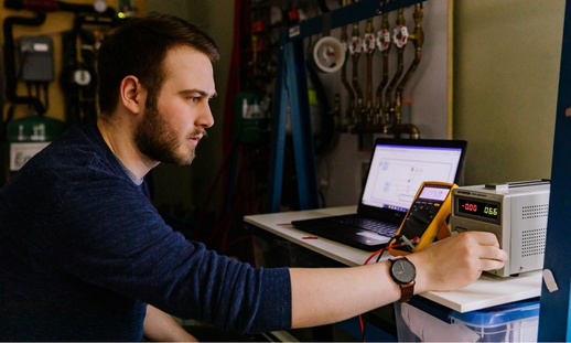 Researcher testing electrical equipment and monitoring system performance in a lab.
