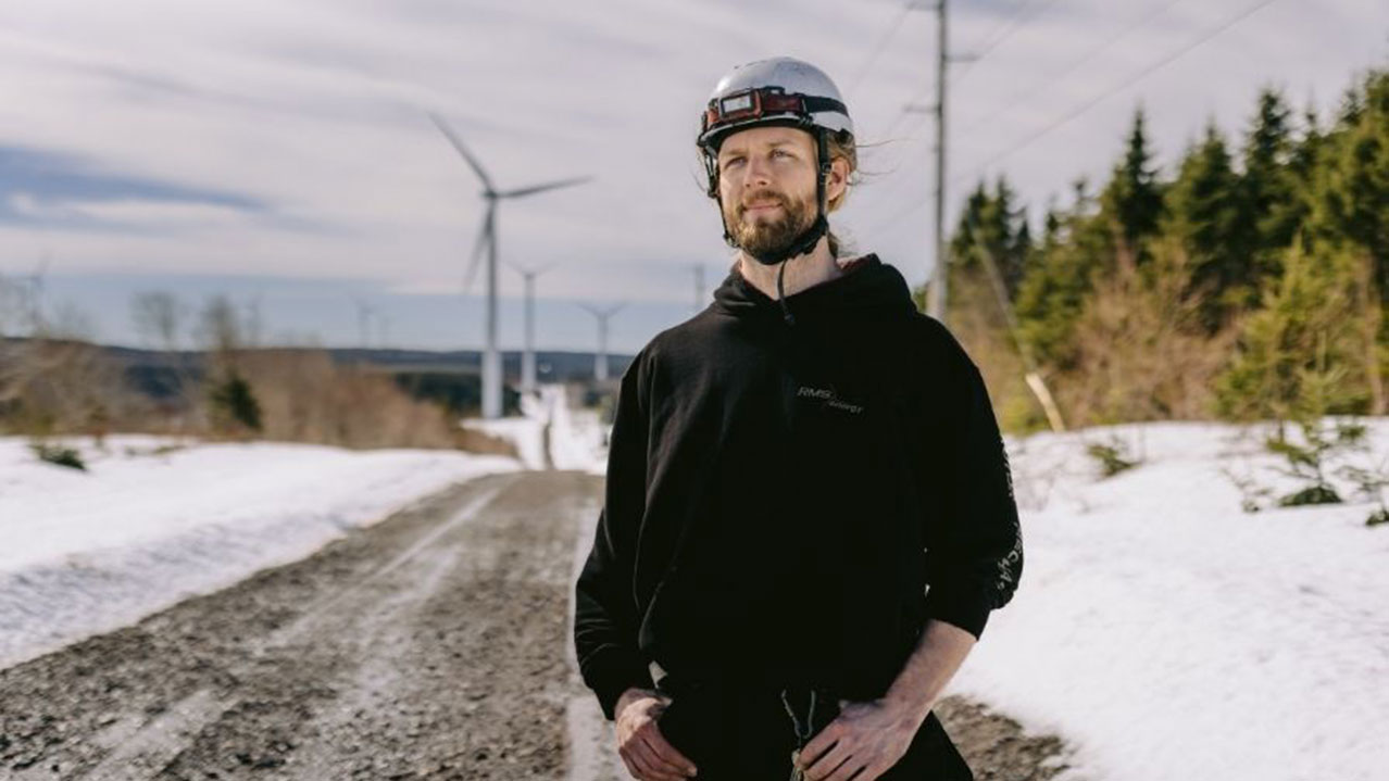 Wind farm worker standing on an access road with wind turbines visible in the background.