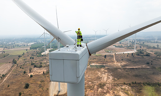 Wind turbine technician standing on top of a wind turbine with multiple turbines visible across the landscape below.