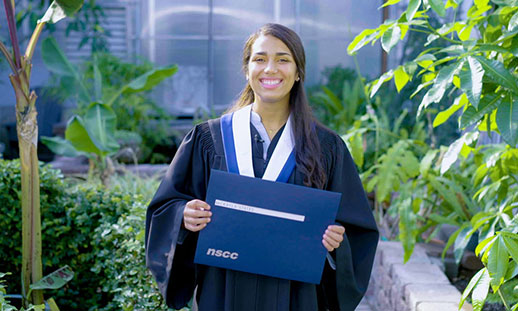 A female wearing a grad gown holding a diploma