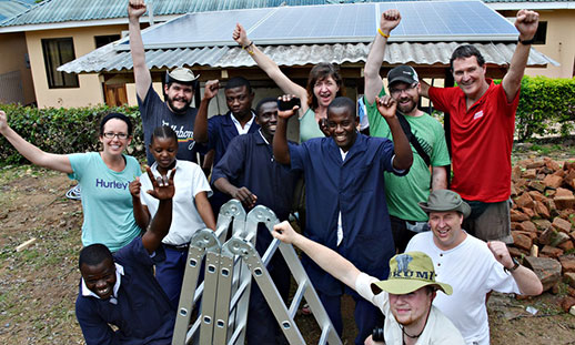 A group of men and women outside cheering in front of a rural school in Africa