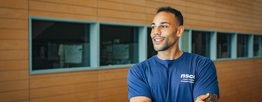 Ty Haley, a Student Services Advisor at Ivany Campus, stands with his arms crossed and smiles as he looks to his right.