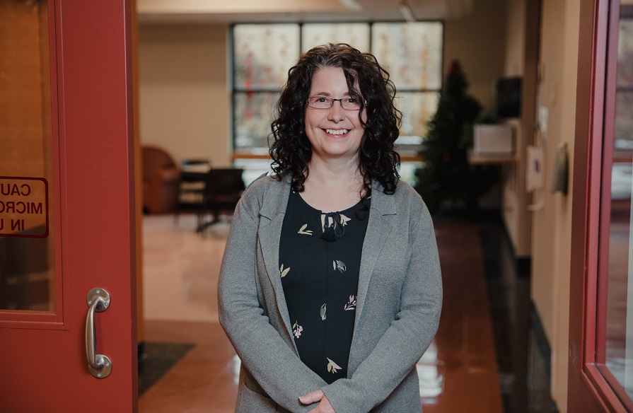 Cathy Mailman, Administrative Assistant, stands facing the camera and smiles.