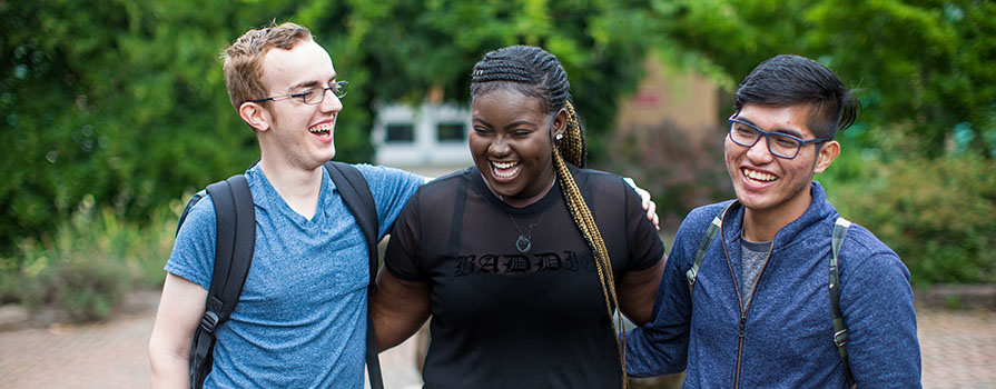 Three students have their arms around each other and are smiling.