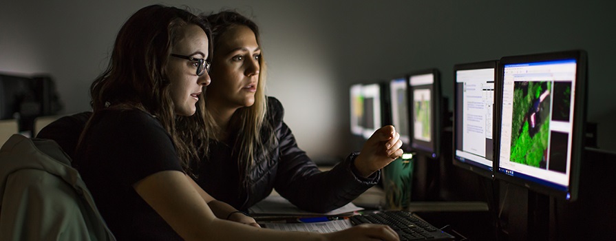 Two female students looking at geomatics data on several computer screens.