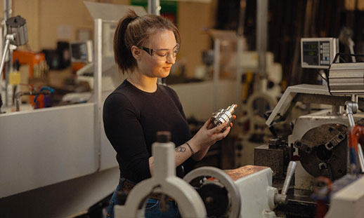 A female precision machining student wearing eye protection working with a machine. 