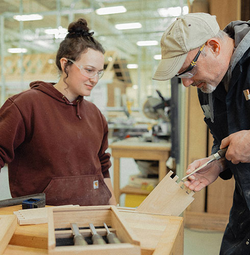 An NSCC student learns woodworking skills from an instructor in a shop setting.