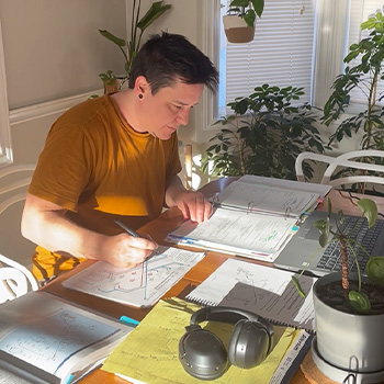 Reese at home sitting at a table with a laptop and papers in front of him
