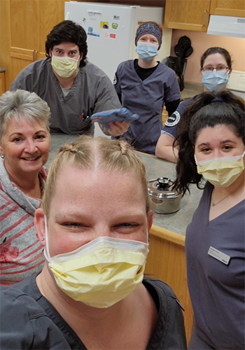 Andrea stands in a kitchen with her classmates and they smile at the camera for a group selfie.