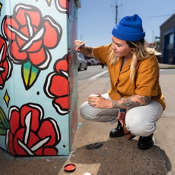 Anisa Francoeur squats down on the sidewalk to paint flowers on an outdoor art installation.