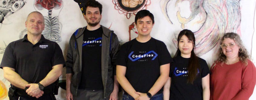 Five individuals stand in front of a wall smiling at the camera.