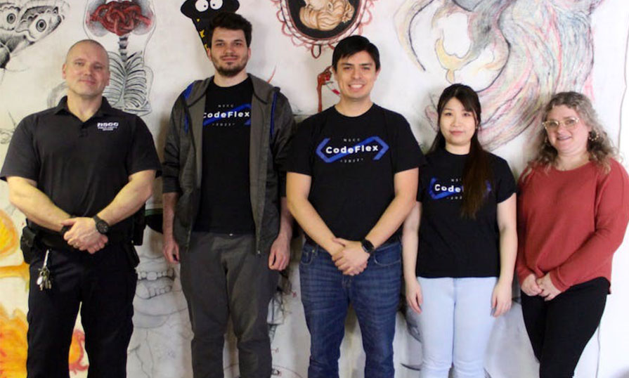 Five individuals stand in front of a wall smiling at the camera. 