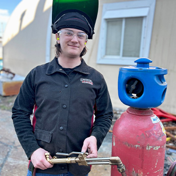 Austin standing outside wearing safety gear and holding a tool
