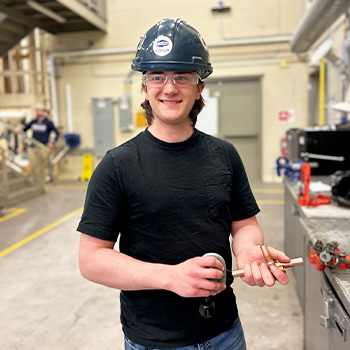 Austin standing in the pipe trades shop smiling at the camera