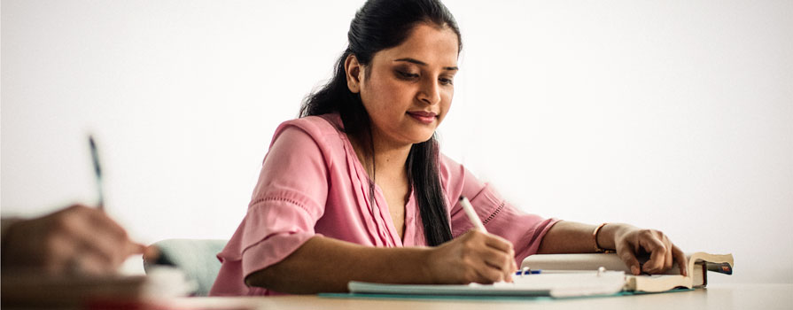 A woman sits at a desk and writes in a notebook.