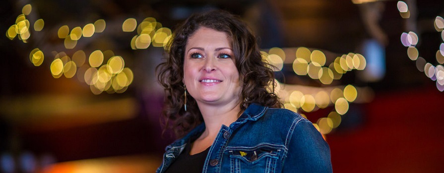 A woman in a jean jacket smiles and looks to the left. The background it blurry.