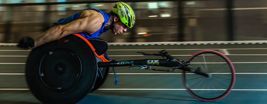 A man in a racing wheelchair is racing around a track. 