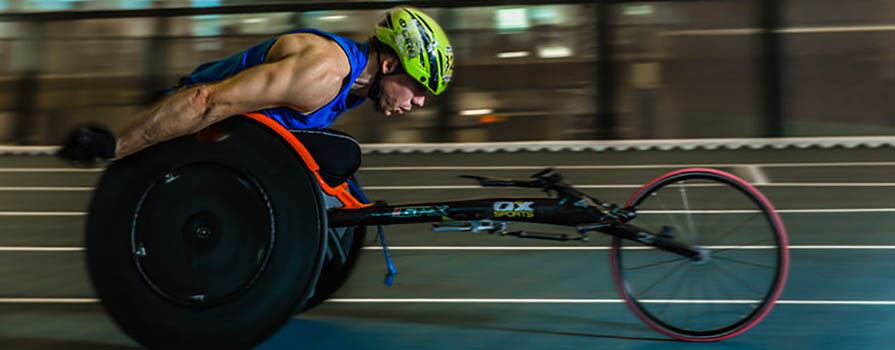 A man in a racing wheelchair is racing around a track.
