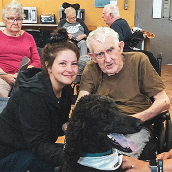 Senior and volunteer sitting posing behind a black dog