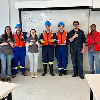 Marine students stand in a row with their thumbs up