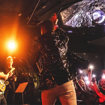 A person is standing on stage behind photographed from behind while singing to an audience.