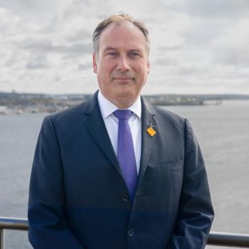 Image of David Benoit, NSCC's new President. He is standing in front of a body of water, wearing a navy suit.