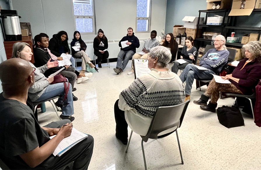 Many people sit around in a circle, debriefing together after the Dementia Live simulation.
