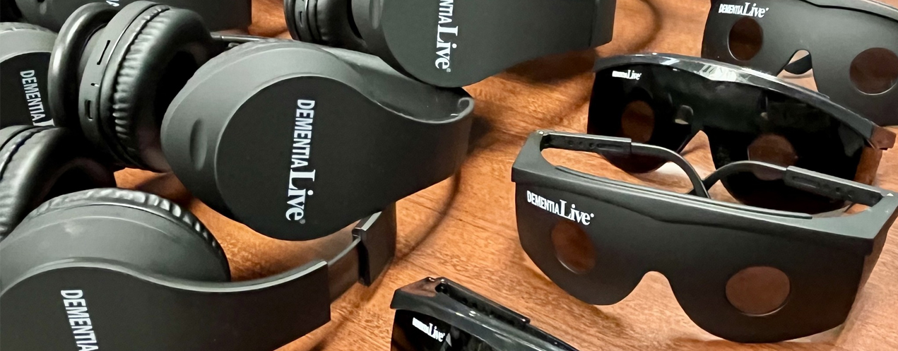 Image shows black headphones and glasses that have a logo on them that reads 'Dementia Live.'