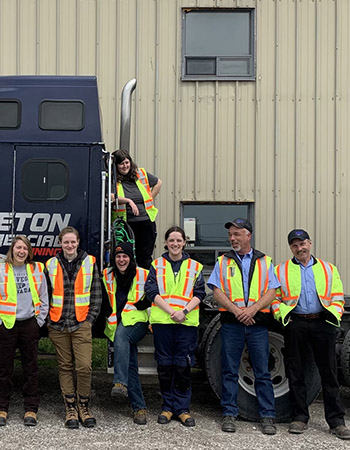 Ellen and her classmates pose on a big rig and smile at the camera.