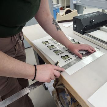 Image shows a student measuring out a print material before cutting it into its proper size.
