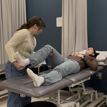 Two Occupational Therapy/Physiotherapy Assistant students practice their mobility techniques on one another in their classroom lab space.