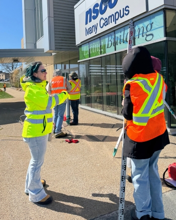 Instructor Amanda assists students with a survey assignment outside Ivany Campus.