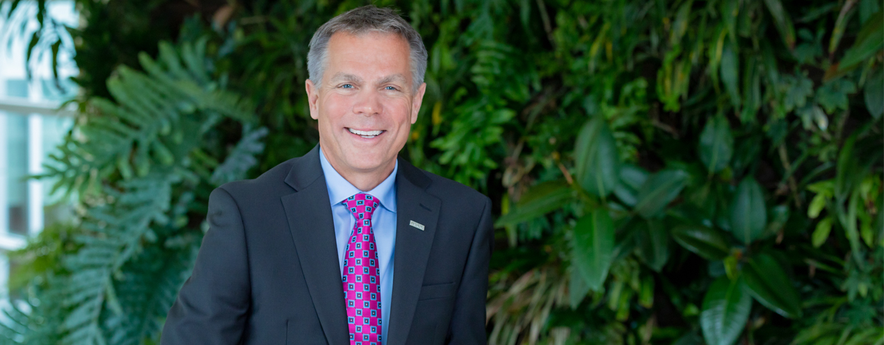 Image shows NSCC President Don Bureaux, smiling at the camera, standing in front of a live living wall.