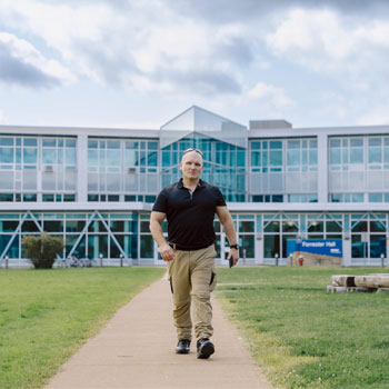 A person is walking down a pathway outside of a glass building.