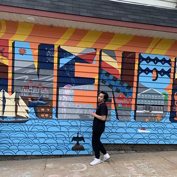 Gabe poses in front of a colourful mural that reads "Lunenburg".