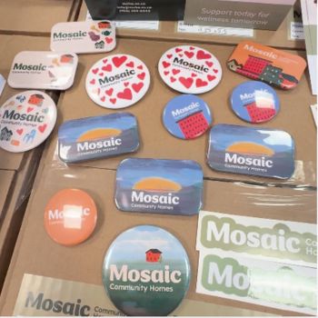 Image shows branded pins, stickers and business cards for Mosaic Community Homes Association.