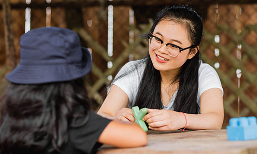 Amelia Dinh, an early childhood educator, smiles at a child in her care across a picnic table.