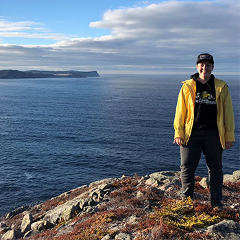 A person is standing on a cliff, overlooking the ocean with ice burgs in the background.