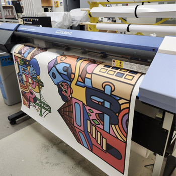 Image shows a large colourful banner being printed from a machine.
