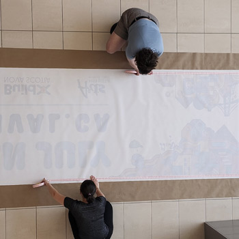 Two people are measuring a new banner on the floor, preparing it to be printed and delivered to the client. 