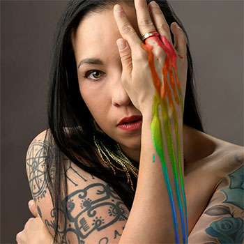 A person is looking at the camera with rainbow paint covering their hands.