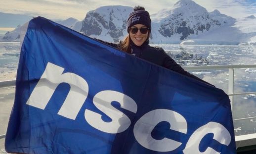 Image of a woman holding an NSCC flag in Antarctica.