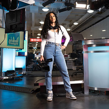 A person is standing in a broadcasting room holding a large filming camera.