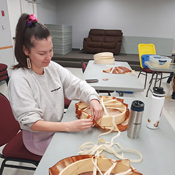 A woman sits at a table making a traditional drum.