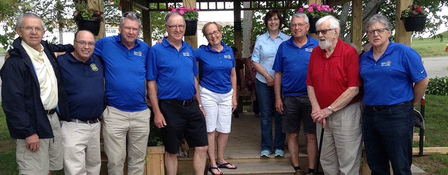 A group of individuals in warm-weather clothing stand in front of a newly constructed gazebo.