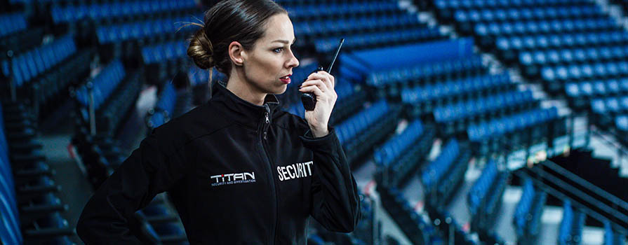 A woman in a security uniform, speaks into a walkie talkie in an empty stadium.