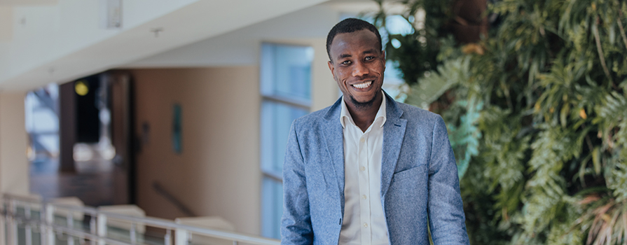 Mashud Zebo, an NSCC graduate, stands in front of the green wall at Institute of Technology Campus and smiles.